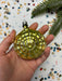 A hand holding a shiny, golden-colored ornament against a background of colorful confetti.