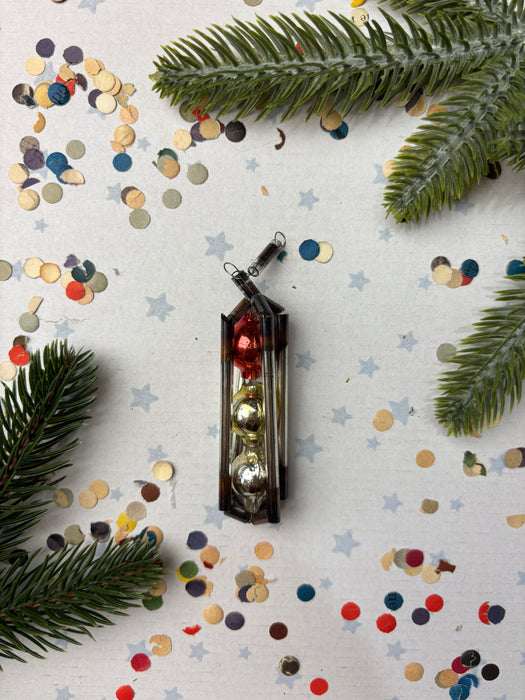a Christmas ornament with red and gold ornaments, surrounded by pine branches and confetti on a white background.