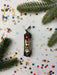 a Christmas ornament with red and gold ornaments, surrounded by pine branches and confetti on a white background.