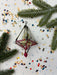 a Christmas ornament with a red ribbon and a small red ball, surrounded by pine branches, confetti, and scattered small circles on a white background.
