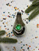 A shiny, metallic ornament with a green gemstone is surrounded by colorful confetti on a white background.