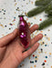 A hand holding a pink, shiny ornament with a small white center, surrounded by colorful confetti on a festive background.