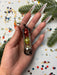 A hand holding a small metal box with colorful balls inside, surrounded by confetti and pine branches.