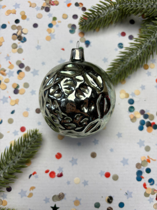 a shiny silver ornament with a reflective surface, surrounded by colorful confetti and green pine branches.