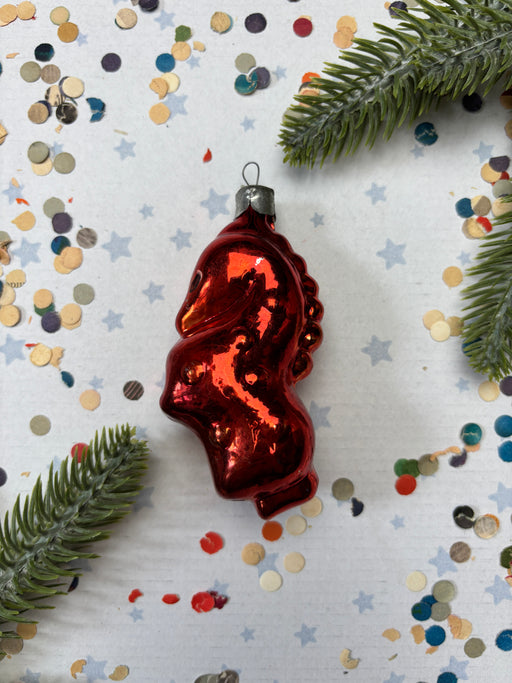 A red ornament resembling a heart shape is placed on a white background with scattered confetti and pine branches.
