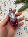 A hand holding a purple and pink ornament against a background of colorful confetti.
