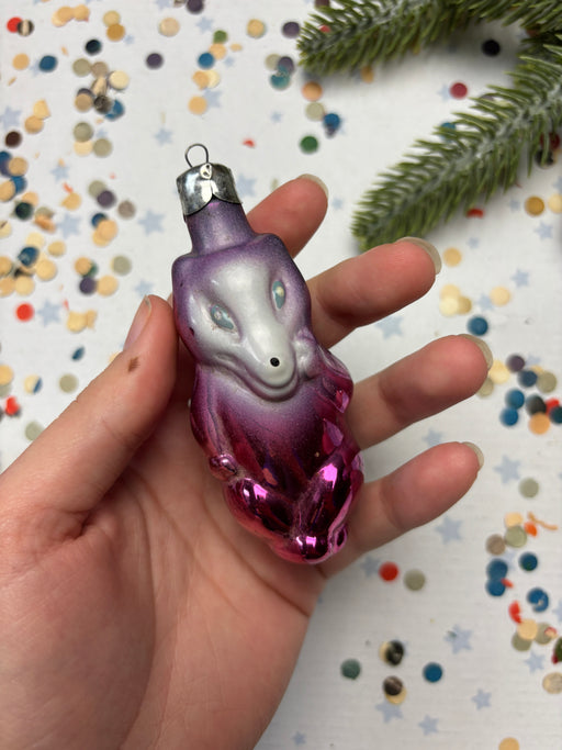A hand holding a purple and pink ornament against a background of colorful confetti.