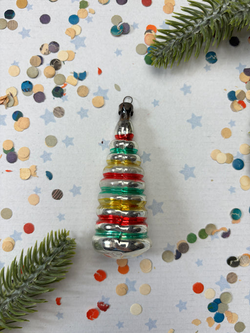 A colorful Christmas ornament with a star-shaped design is surrounded by confetti and a green plant leaf on a white background.