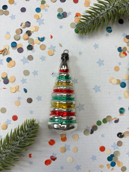 A colorful Christmas ornament with a star-shaped design is surrounded by confetti and a green plant leaf on a white background.