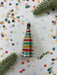 A colorful Christmas ornament with a star-shaped design is surrounded by confetti and a green plant leaf on a white background.