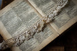 An open book with a delicate lace bookmark resting on its pages, accompanied by a small metal charm in the shape of a rabbit.