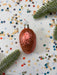 A shiny, metallic ornament in the shape of a brain is surrounded by colorful confetti and a sprig of greenery on a white background.