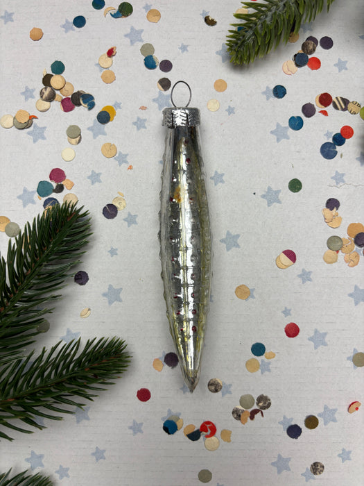 a silver ornament with a pointed end, surrounded by colorful confetti and pine branches.