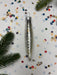 a silver ornament with a pointed end, surrounded by colorful confetti and pine branches.