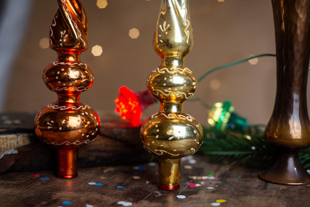 two ornate golden ornaments, one red and one gold, placed on a wooden surface with scattered confetti around them.