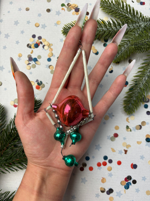 A hand holding a red ornament with green and silver accents, surrounded by Christmas decorations and confetti.