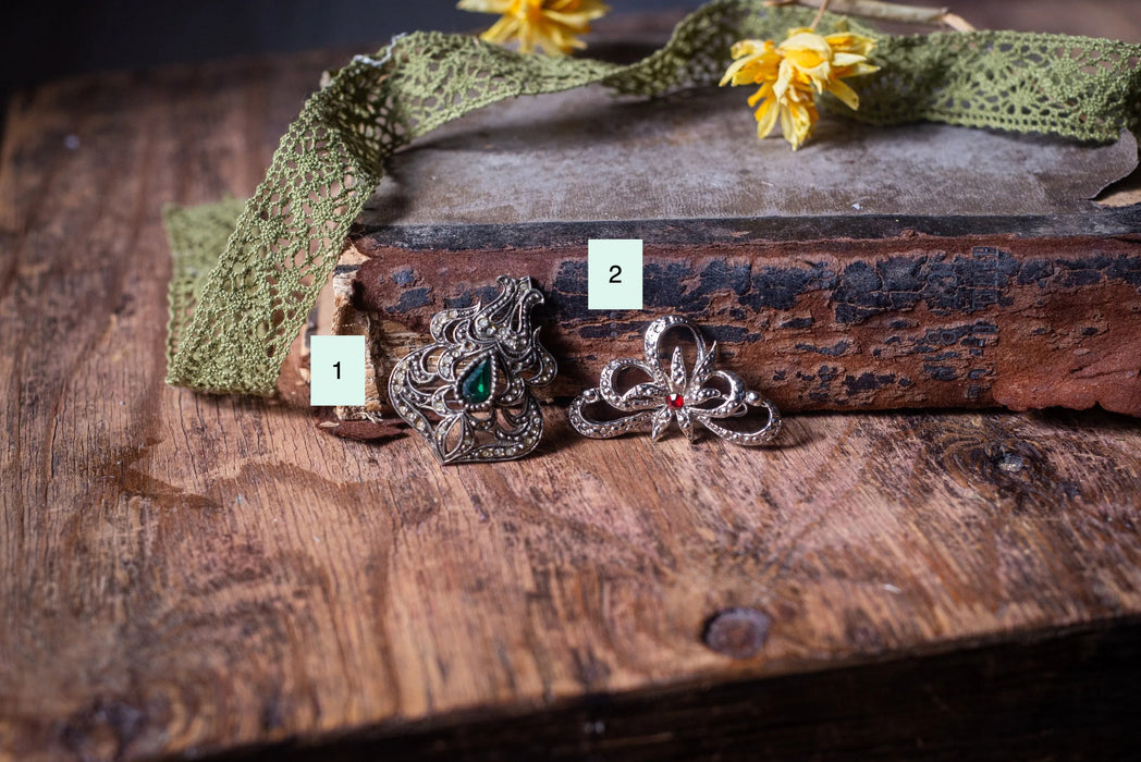 three ornate brooches with intricate designs, placed on a wooden surface alongside a green lace ribbon.