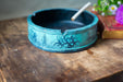 A blue ashtray with a white cigarette in it, placed on a wooden surface next to a book.