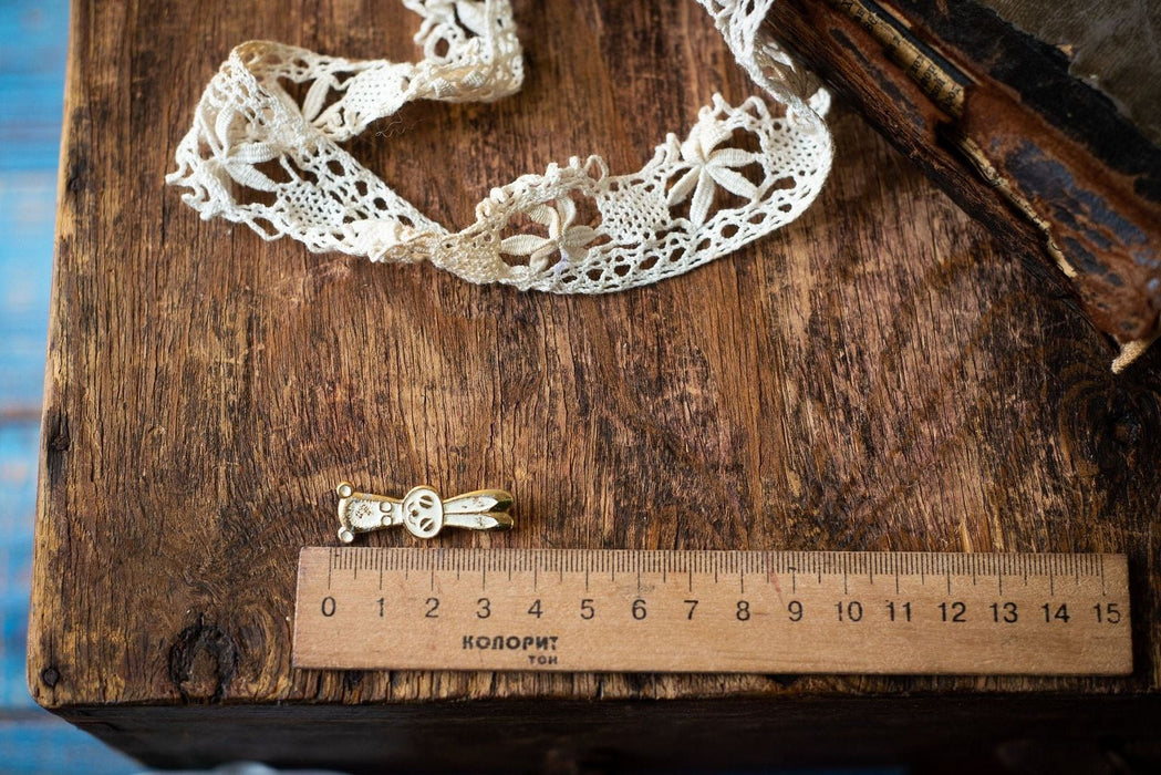 a wooden ruler with a scale ranging from 0 to 15 centimeters, placed on a wooden surface alongside a piece of white lace and a small golden pin.