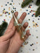 A hand holding a glass ornament with a floral design, surrounded by colorful confetti and pine branches.