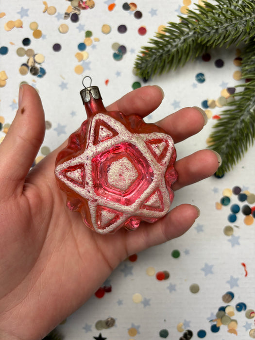 A hand holding a pink star-shaped ornament with a star design, surrounded by colorful confetti on a festive background.