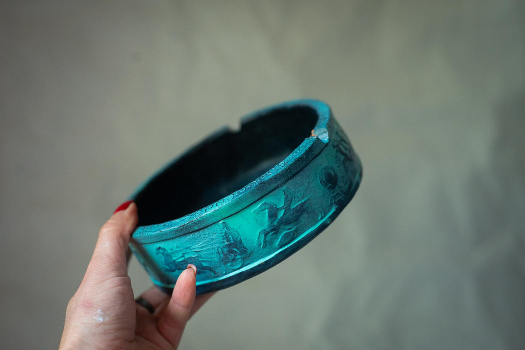 A hand holding a blue ashtray with a decorative design on it.