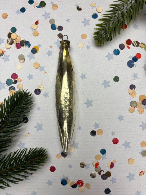 a shiny gold ornament with a pointed end, surrounded by colorful confetti and pine branches.