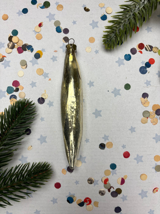 a shiny gold ornament with a pointed end, surrounded by colorful confetti and pine branches.
