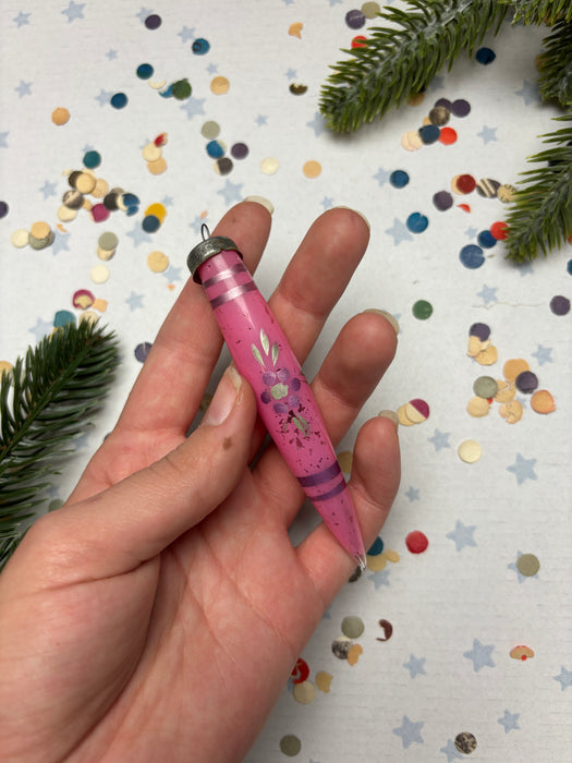 A hand holding a pink crayon with a floral design, surrounded by colorful confetti on a white background.