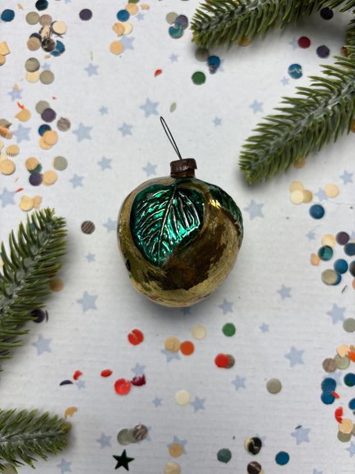a Christmas ornament with a green leaf on it, surrounded by confetti and pine branches.