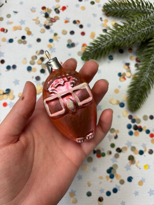 A hand holding a small, orange ornament with a red and white design, surrounded by colorful confetti on a white background.