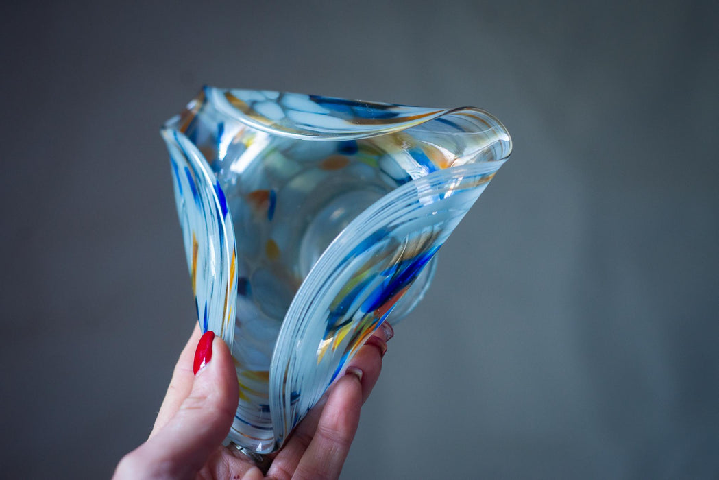 A hand holding a colorful glass sculpture against a gray background.