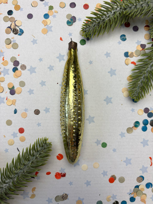a shiny, metallic object, possibly a piece of jewelry or a decorative item, placed on a background of confetti and green leaves.