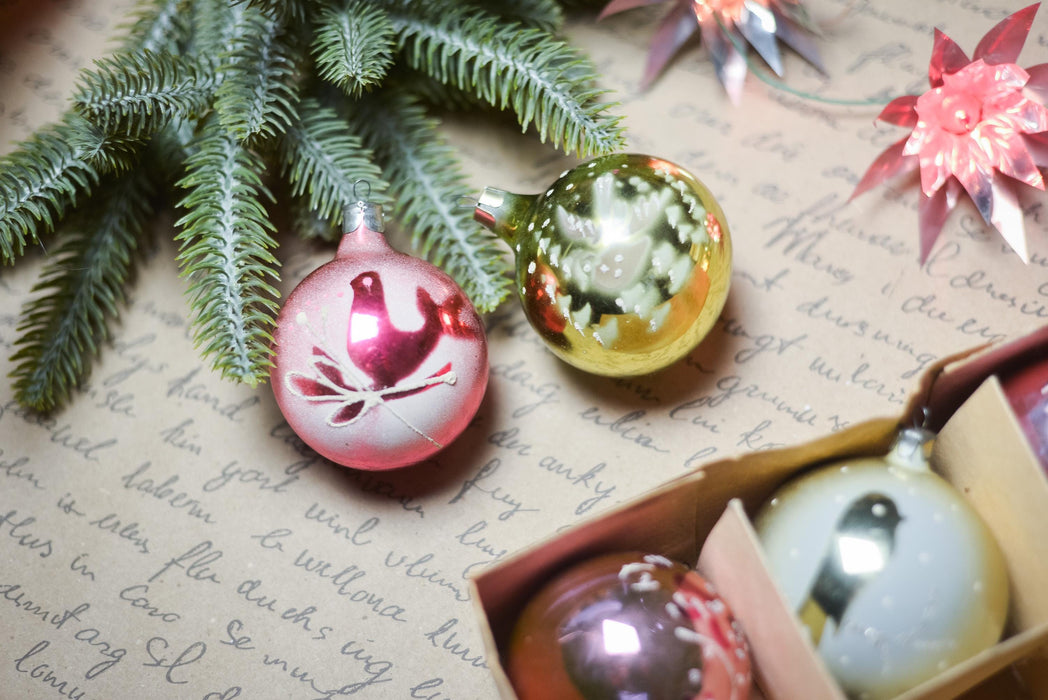 Christmas ornaments, including a pink bird ornament, a yellow ornament, and a white ornament, placed on a piece of paper with handwritten text.