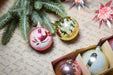 Christmas ornaments, including a pink bird ornament, a yellow ornament, and a white ornament, placed on a piece of paper with handwritten text.
