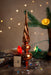 a Christmas tree ornament with a twisted design, surrounded by holiday decorations such as a pine branch, twinkling lights, and confetti on a wooden surface.
