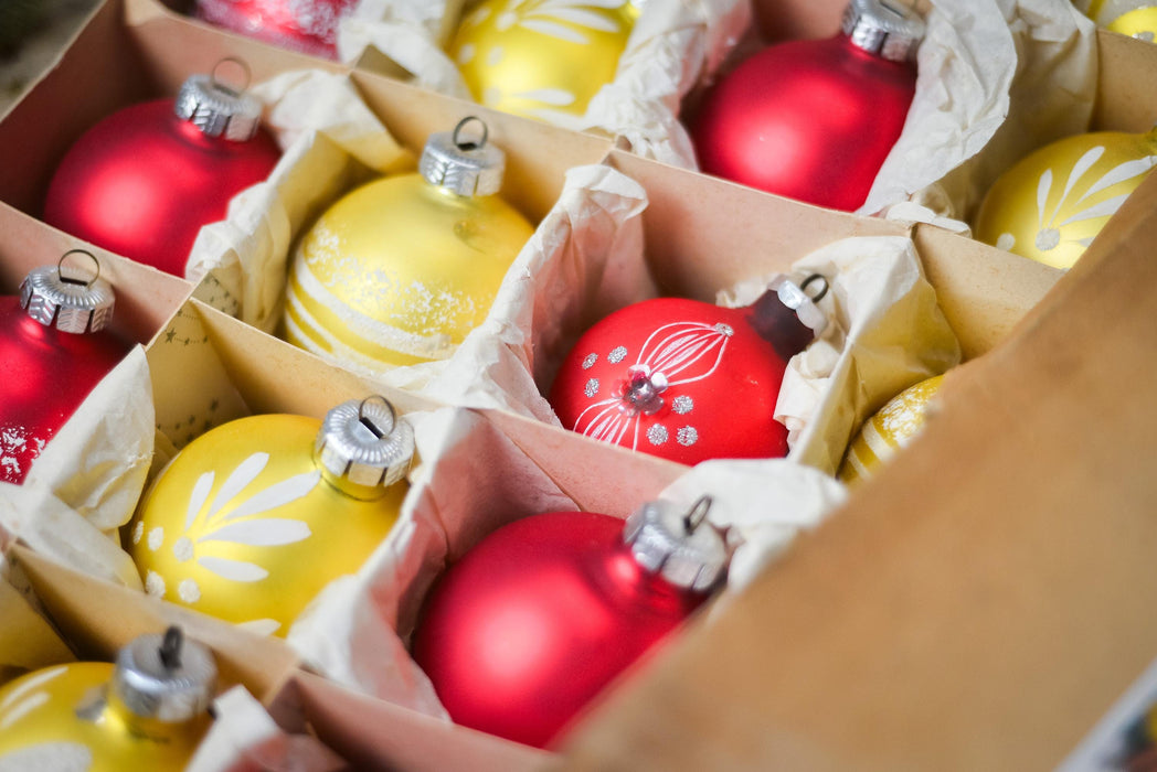 A cardboard box filled with various Christmas ornaments, including red and yellow balls, arranged in rows.