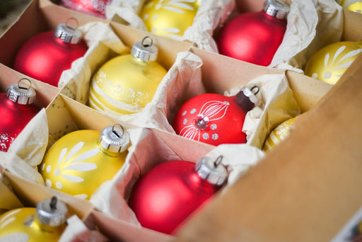 A cardboard box filled with various Christmas ornaments, including red and yellow balls, arranged in rows.
