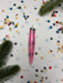 a pink pen with a floral design, surrounded by colorful confetti and pine branches.