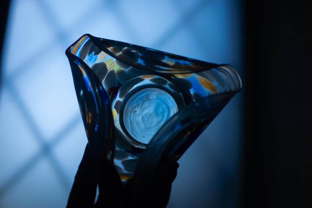 A close-up view of a glass vase with a colorful, abstract design, held in a person's hand against a dark background.
