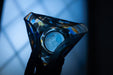 A close-up view of a glass vase with a colorful, abstract design, held in a person's hand against a dark background.