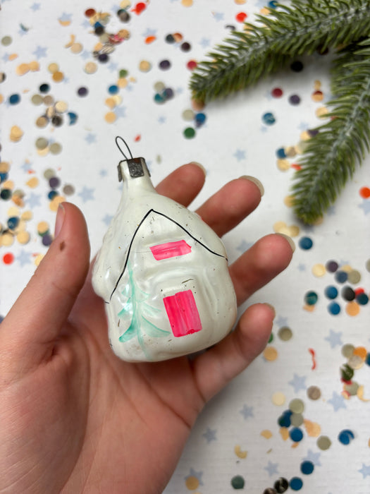 A hand holding a white ornament with a pink and green design, against a background of colorful confetti.