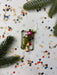 a festive scene with Christmas decorations, including a Christmas tree branch, ornaments, and confetti scattered across a white background.