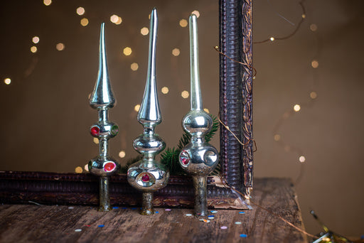three decorative ornaments with pointed tops, placed on a wooden surface against a background of twinkling lights.
