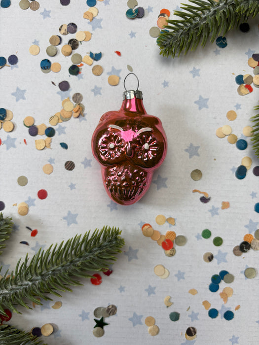 A pink Christmas ornament with a star design sits on a background of colorful confetti and pine branches.