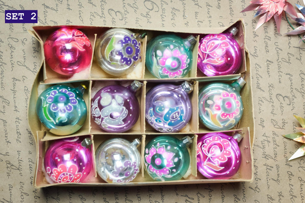 A cardboard box containing a dozen ornaments with various colorful designs, including flowers and geometric patterns.