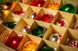 A close-up view of a collection of colorful Christmas ornaments arranged in a box, with a blurred background suggesting a festive setting.