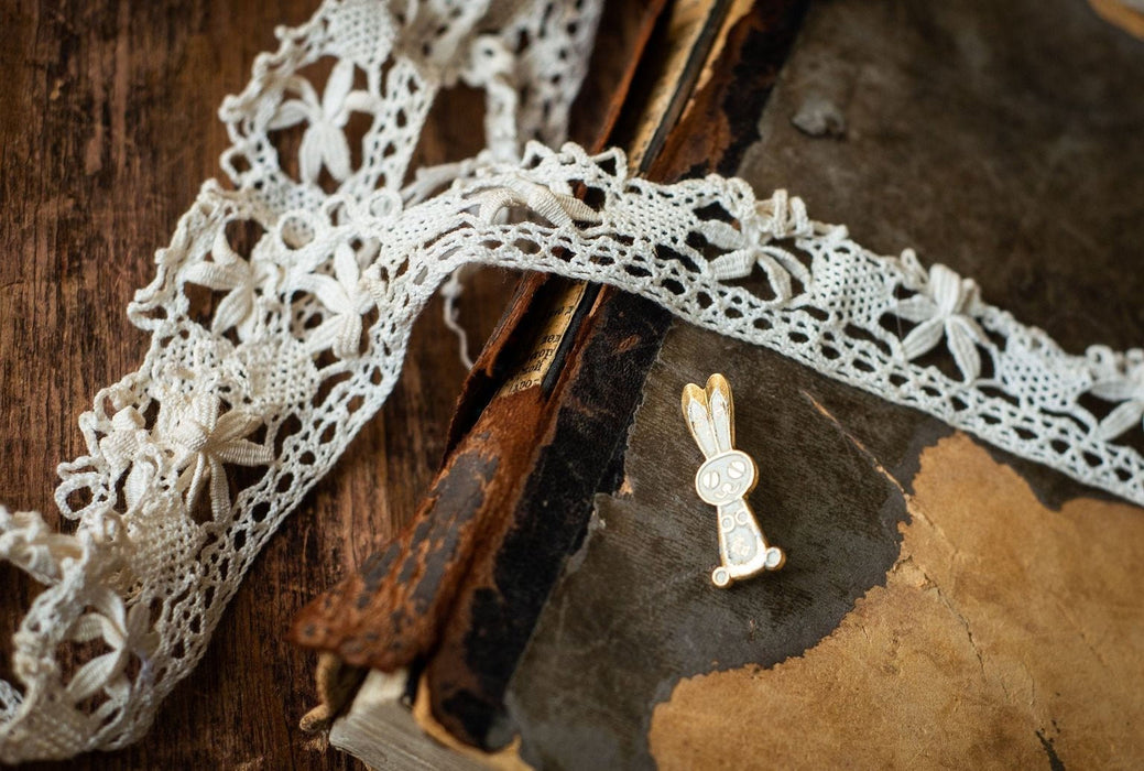 a close-up of a small, ornate pin with a rabbit design, resting on a worn, aged book with a lace-like pattern.