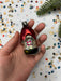 A hand holding a small, colorful ornament against a background of confetti and a pine branch.