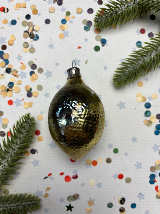 a shiny, metallic ornament with a textured surface, surrounded by colorful confetti and a sprig of greenery.